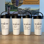 Four white insulated carry mugs with black lids and handles are lined up on a wooden tabletop in front of a branded product display sign. The mugs have printed text reading 'My Coffee Order' with various drink combinations listed below.