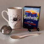 Tea set with a mug, tea box, spoon, and tea strainer on a gray background