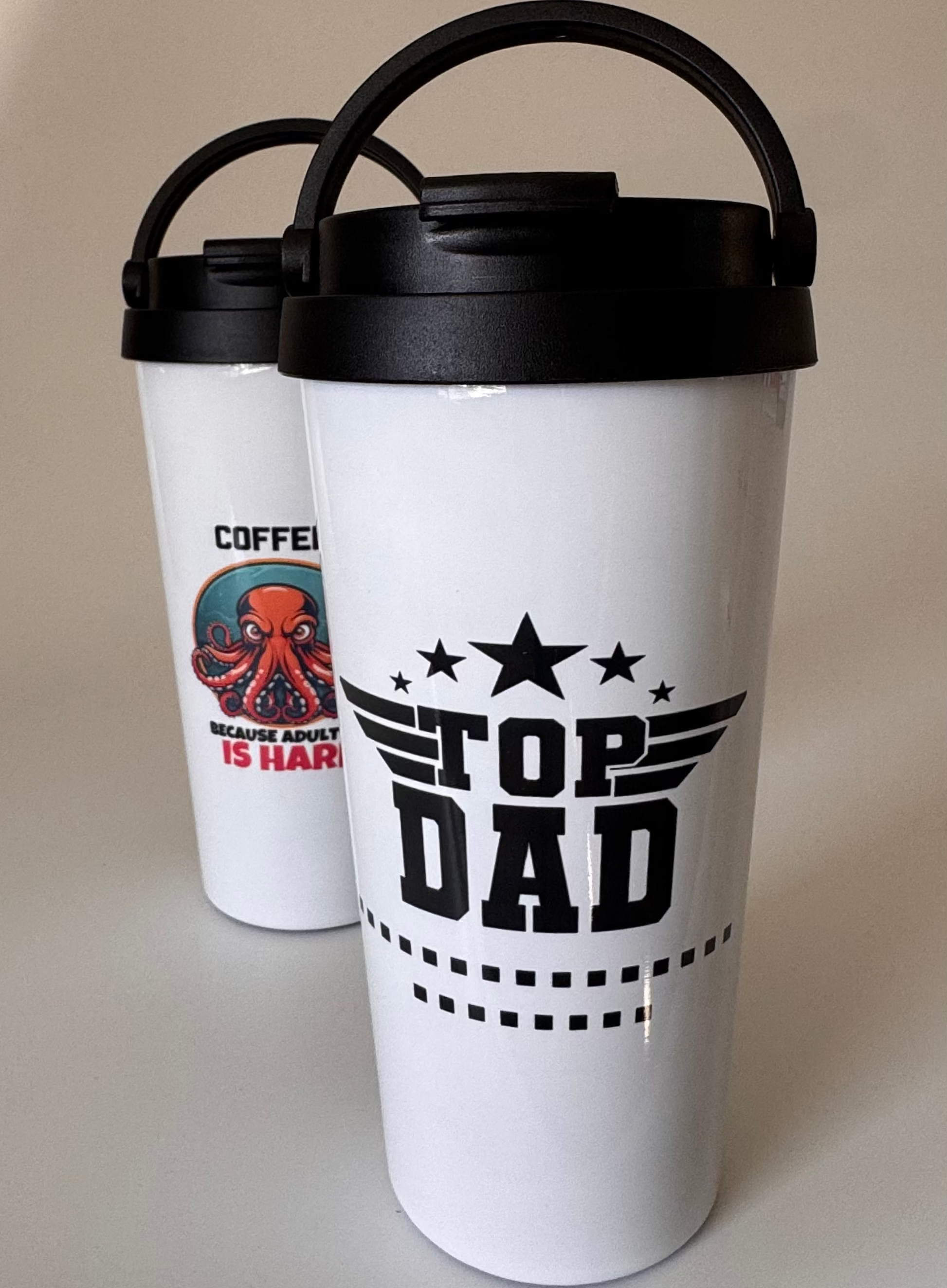 Two white tumblers with black lids, one featuring a graphic of an octopus and text, the other with 'Top Dad' text.