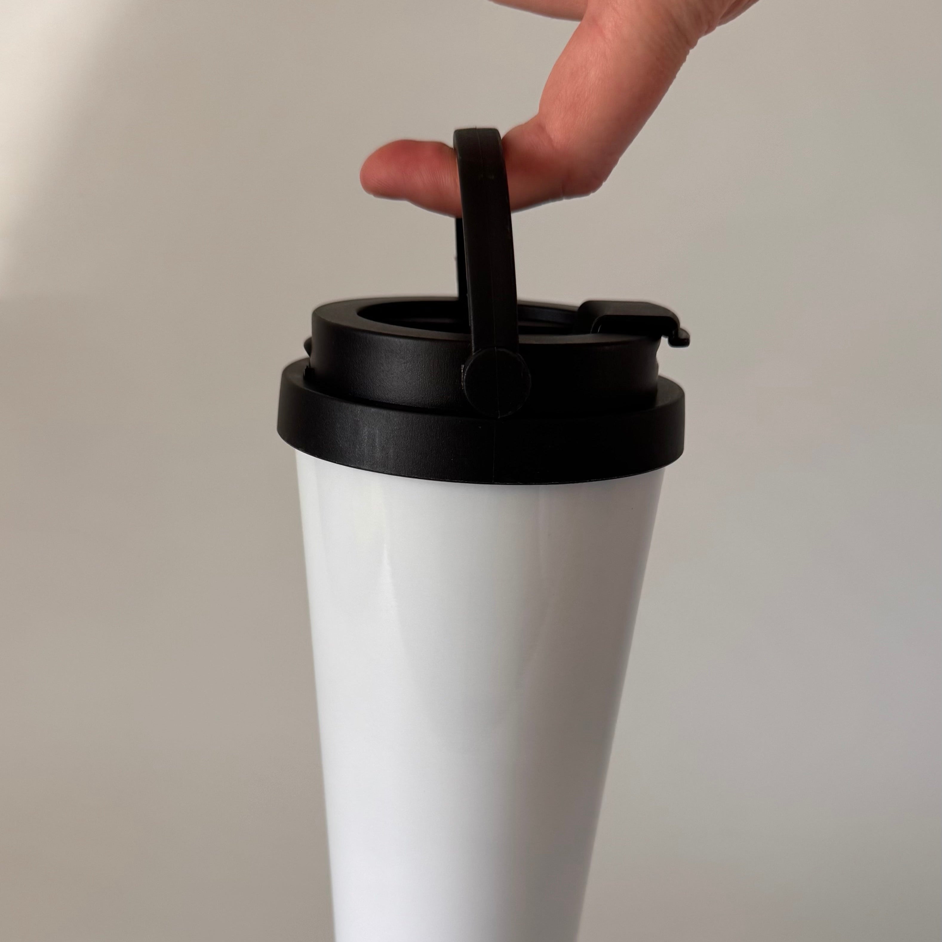 White tumbler with a black lid held by a hand against a plain background
