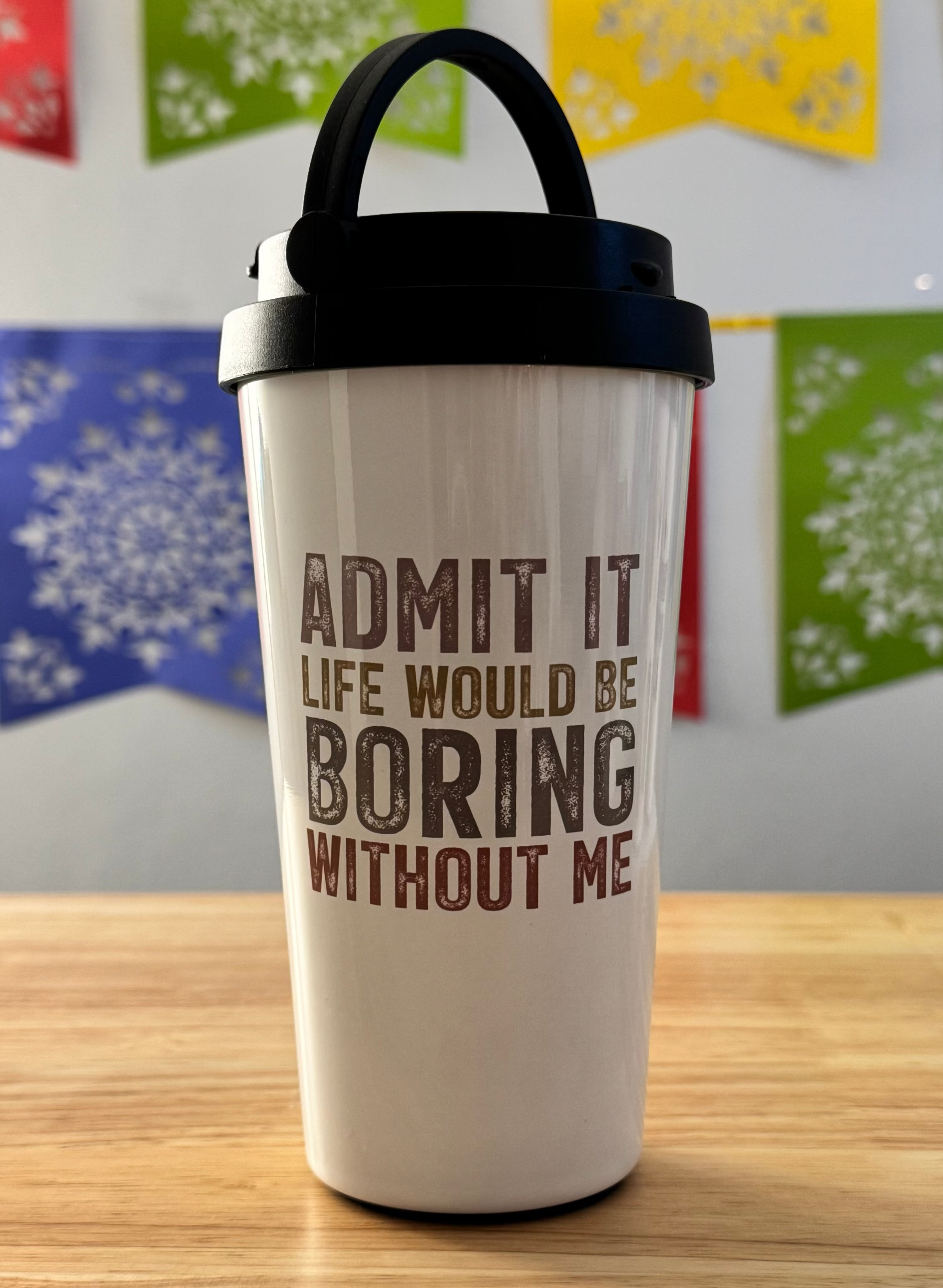 White tumbler with text on a wooden surface with colorful flags in the background