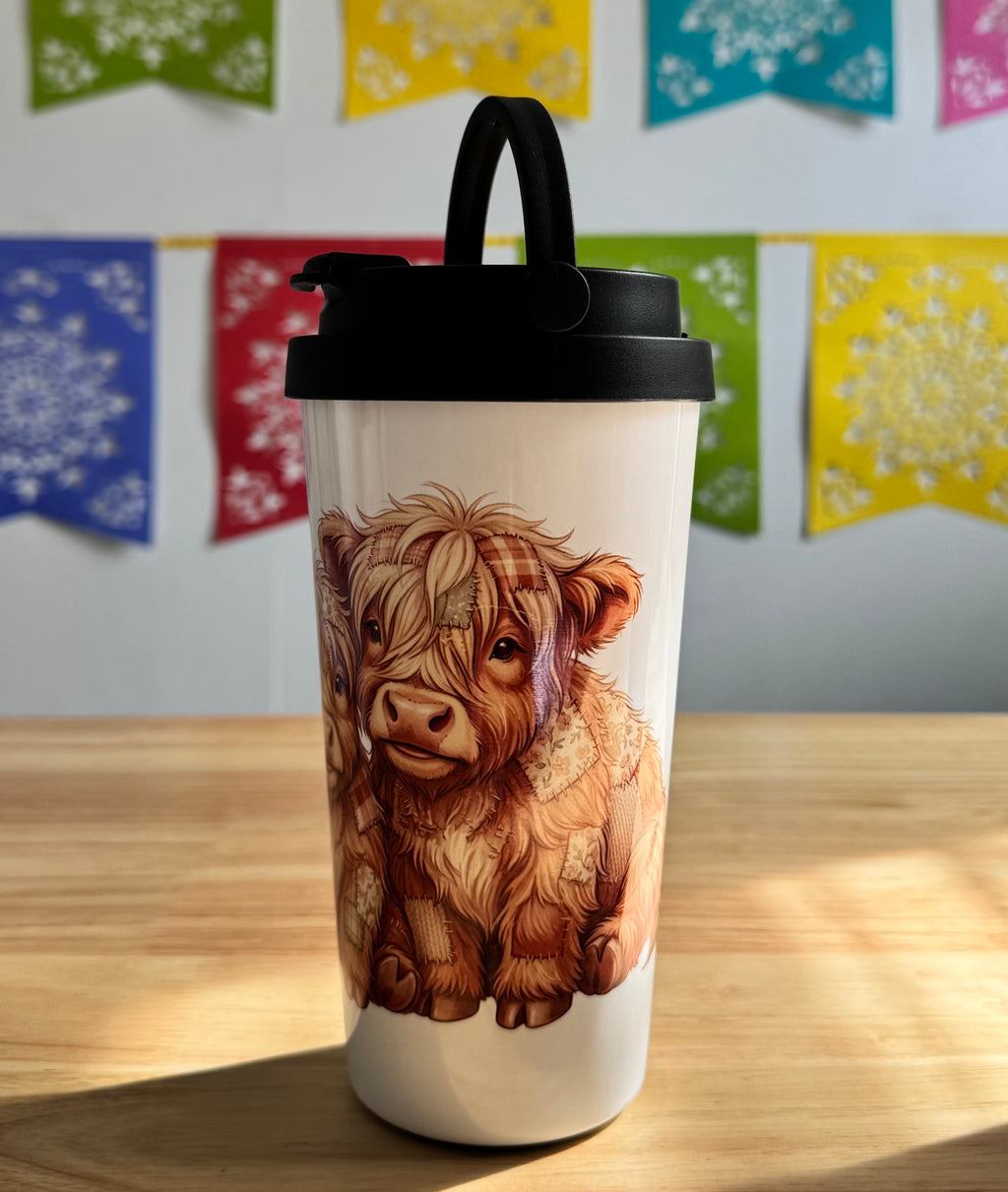 Tumbler with a cow design on a wooden surface with colorful flags in the background