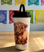 Tumbler with a cow design on a wooden surface with colorful flags in the background