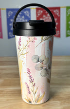 Tumbler with floral design on a wooden surface with colorful flags in the background