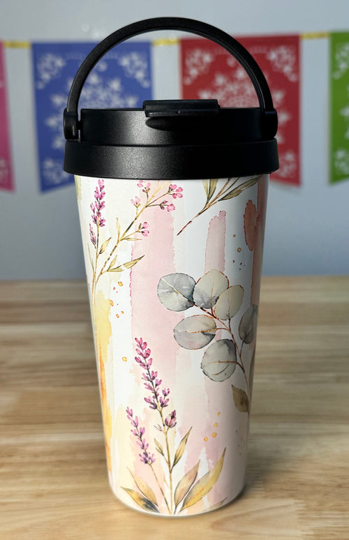 Tumbler with floral design on a wooden surface with colorful flags in the background